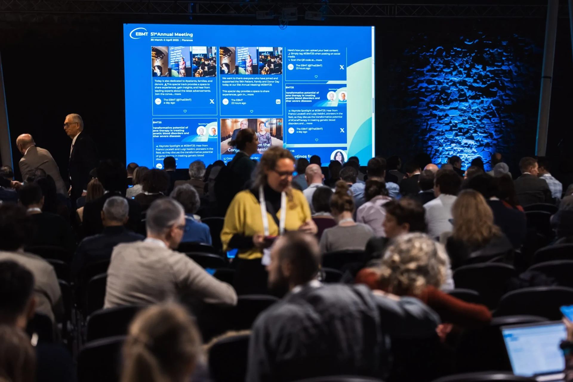 Conference audience seated in a darkened auditorium with an ERN annual meeting social wall projected on the large stage screen