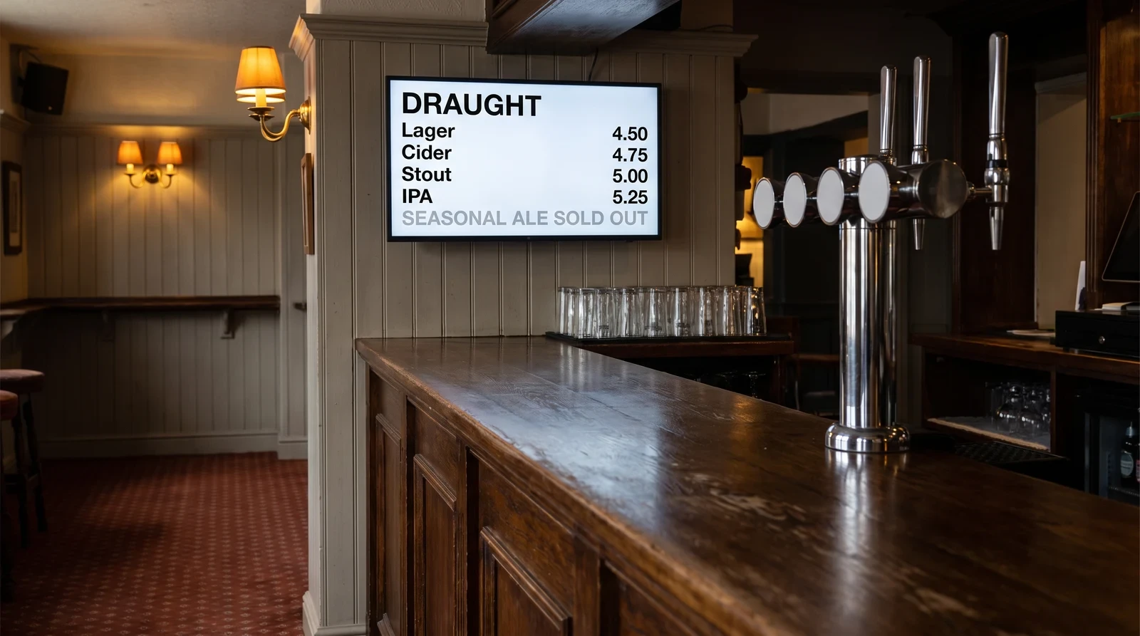 Pub bar counter with a digital draught menu board showing drink prices and one line marked sold out