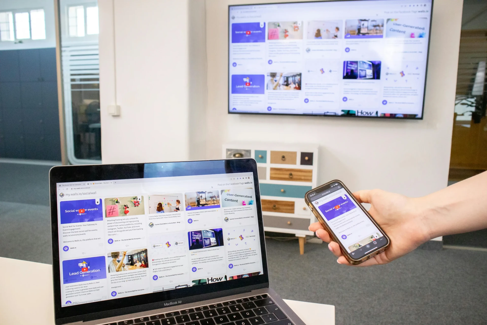 Walls.io dashboard open on a laptop and phone with the connected social wall playing live on a wall-mounted TV