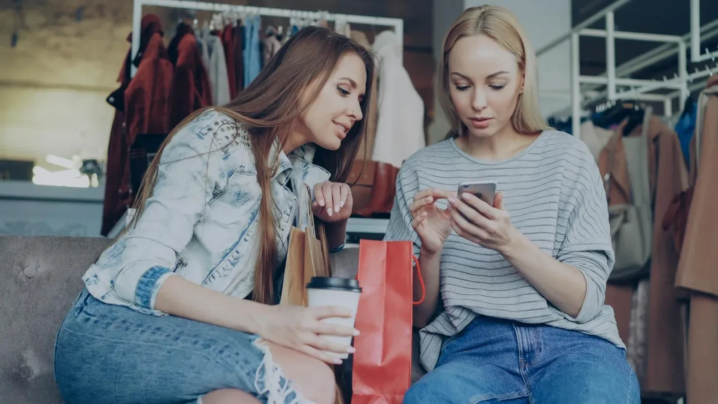 Two women in a clothing store browsing social media together on a phone